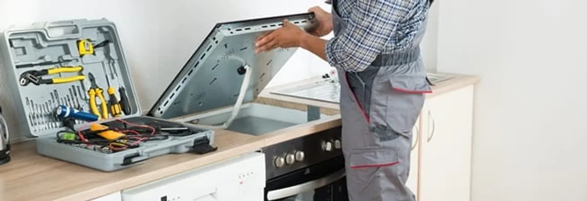 Cooktop repair technician lifting a built-in stovetop for service in Baltimore, MD