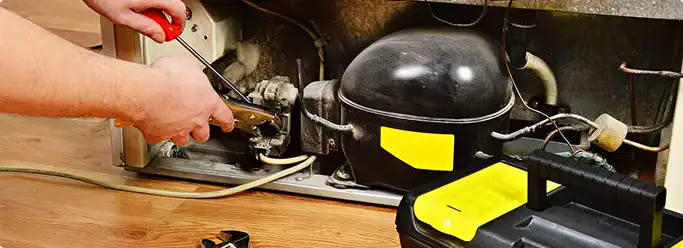 Refrigerator repair technician fixing the compressor and wiring in Baltimore, MD